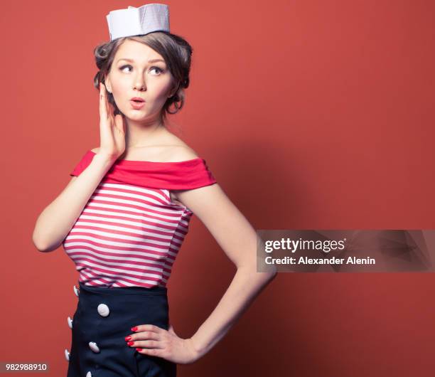 beautiful pin-up girl dressed a sailor posing on red background - pin up girl stockfoto's en -beelden