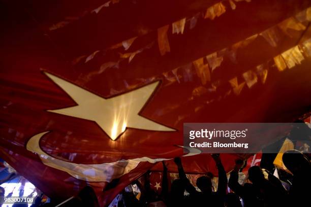People hold a large Turkish national flag outside of the AKP party headquarters as they react to the outcome of the parliamentary and presidential...