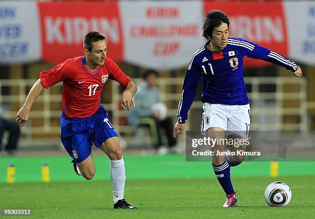 Keiji Tamada of Japan and Aleksandar Davidov of Serbia compete for the ball during the Kirin Challenge Cup match between Japan and Serbia at Nagai...