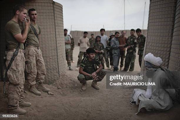 Two US Marines from India Company, 3rd Battalion, 6th Marines, guard an Afghan detainee as an Afghan National Army soldier talks with him, at their...