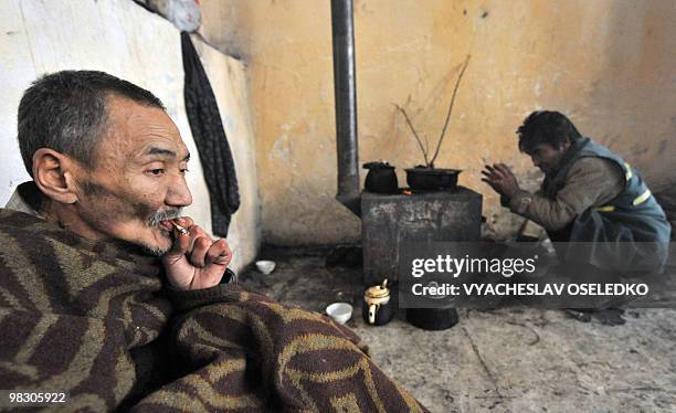 Homeless man huddles under a blanket as another prepares warms himself by a stove at a shelter in the Kyrgyz capital of Bishkek on February 15, 2010....