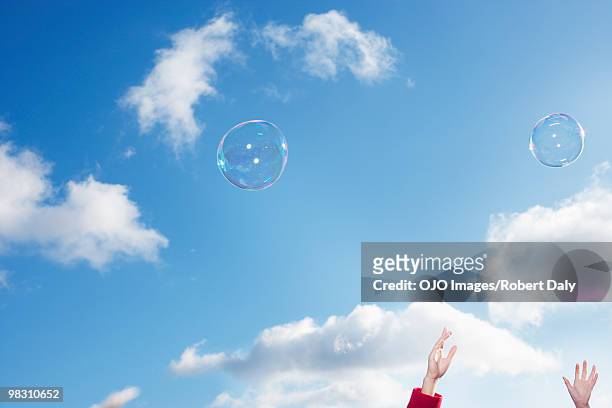 hands reaching for bubbles against blue sky - robert a daly bildbanksfoton och bilder