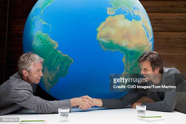 businessmen shaking hands around large globe on conference table - world war 2 stock-fotos und bilder