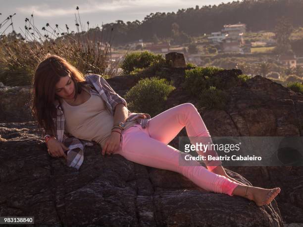 young woman lying on rock with village on hill in background, nigran, pontevedra, galicia, spain - rock hill stock pictures, royalty-free photos & images