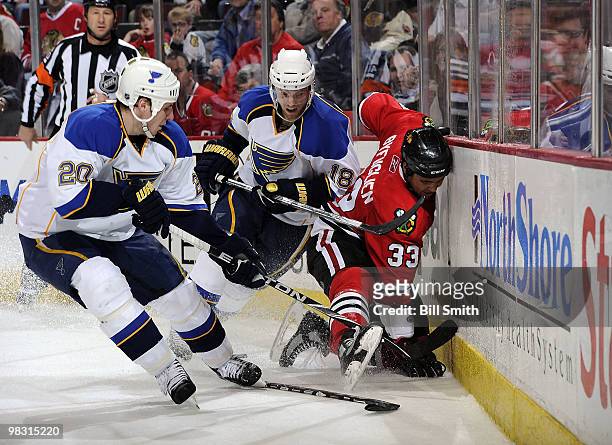 Dustin Byfuglien of the Chicago Blackhawks grabs for the puck as Alexander Steen and Jay McClement of the St. Louis Blues skate in from behind, on...