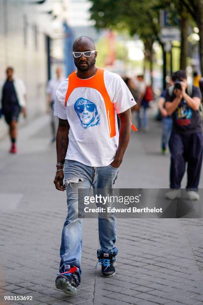 Virgil Abloh, Artistic Director for Louis Vuitton Menswear and Off-White creator, wears a an orange and white t-shirt, ripped denim jeans,...