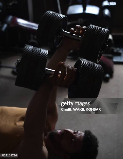 This photo taken on April 9, 2018 shows an Afghan bodybuilder using dumbbells made from spare car parts as he exercises at the Aziz Aruzo...