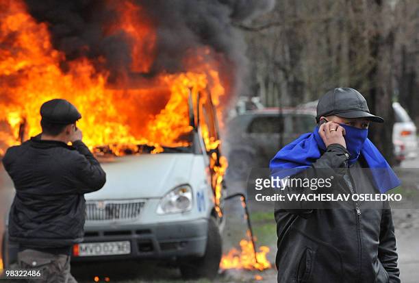 Kyrgyz opposition supporter speaks on a phone infront of a burning vehicle during an anti-government protest in Bishkek on April 7, 2010. Opposition...
