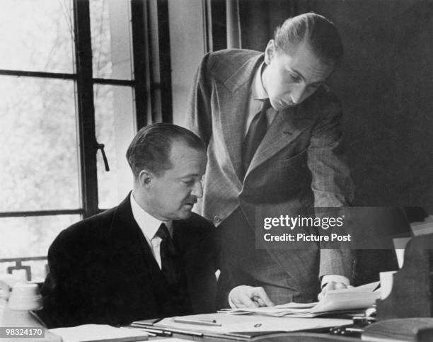 British Conservative politician Afred Duff Cooper, 1st Viscount Norwich , the Minister of Information, at his office, 1940. His secretary is handing...