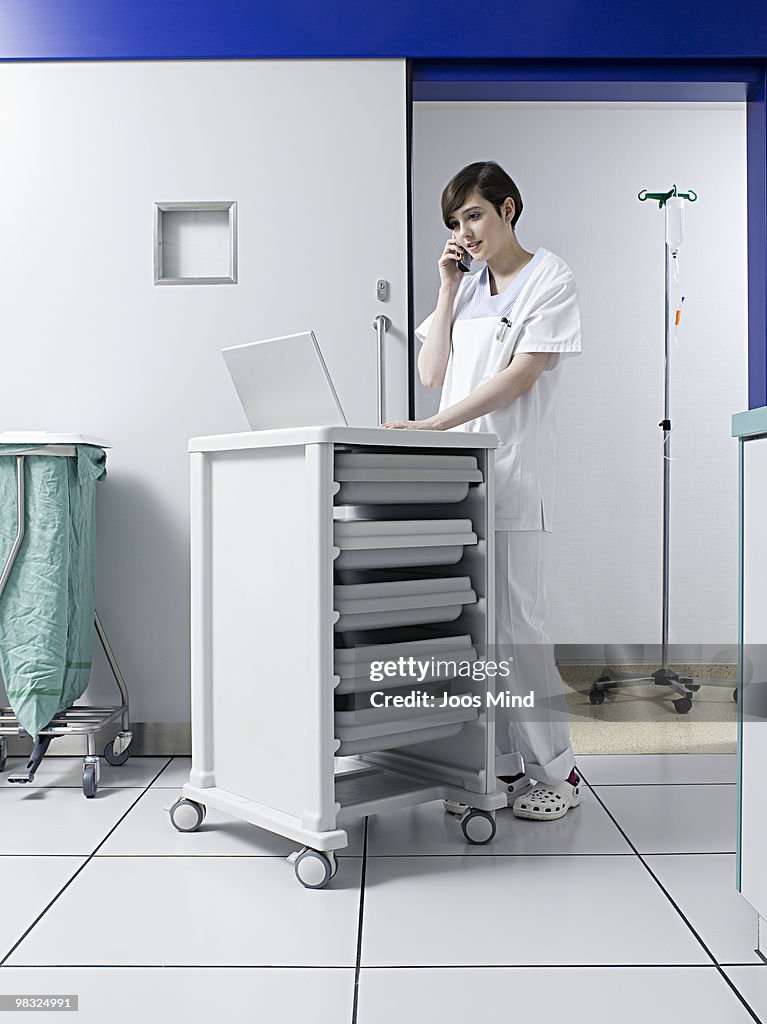 Nurse holding mobile phone, using laptop