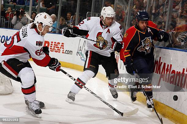 Stephen Weiss of the Florida Panthers digs the puck out from the boards against Erik Karlsson of the Ottawa Senators and teammate Mike Fisher at the...