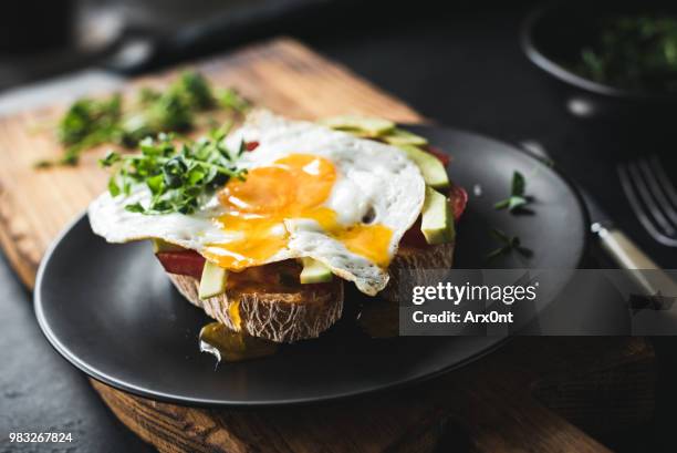 breakfast toast with avocado, fried egg and sprouts - black plate stock pictures, royalty-free photos & images