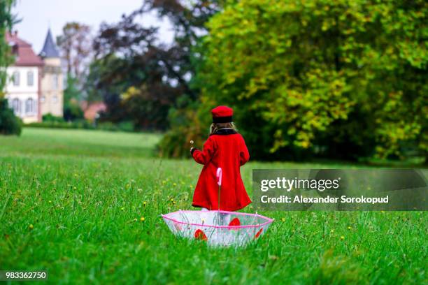 cute little girl dressed in red coat and hat on green grass fiel - green coat - fotografias e filmes do acervo