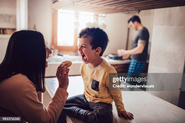 cheerful mother giving little son cookie in the morning - mother's day breakfast stock pictures, royalty-free photos & images