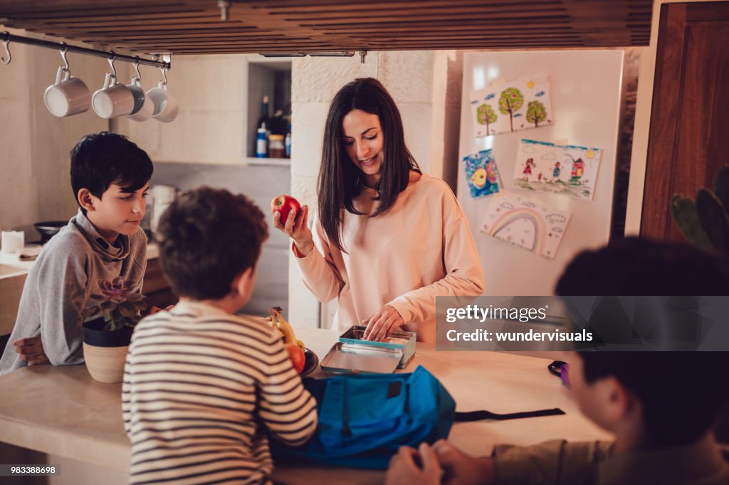 Mother preparing healthy food lunch boxes for children in kitchen