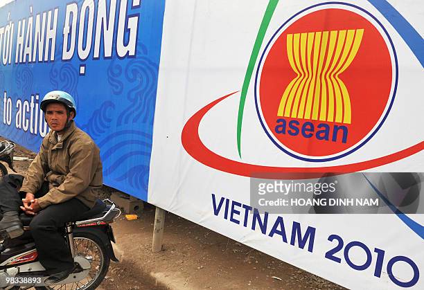 Motorcycle-taxi driver sits waiting for clients next to a poster marking the 16th summit of the Association of Southeast Asian Nations on a road in...