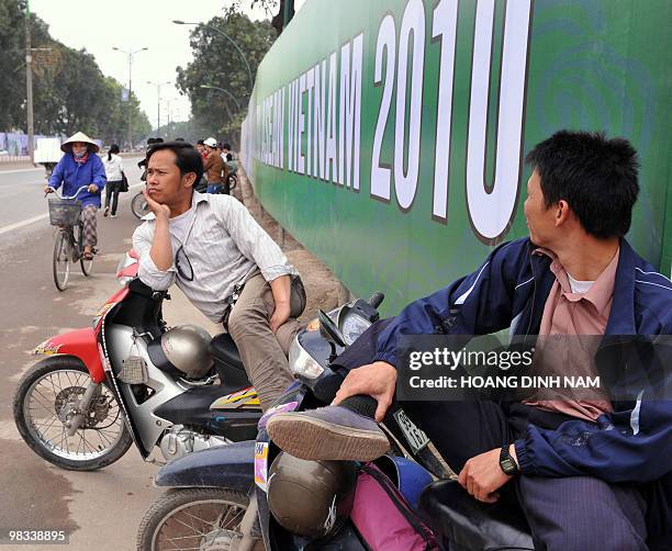 Motorcycle-taxi drivers sit waiting for clients next to a poster marking the 16th summit of the Association of Southeast Asian Nations on a road in...