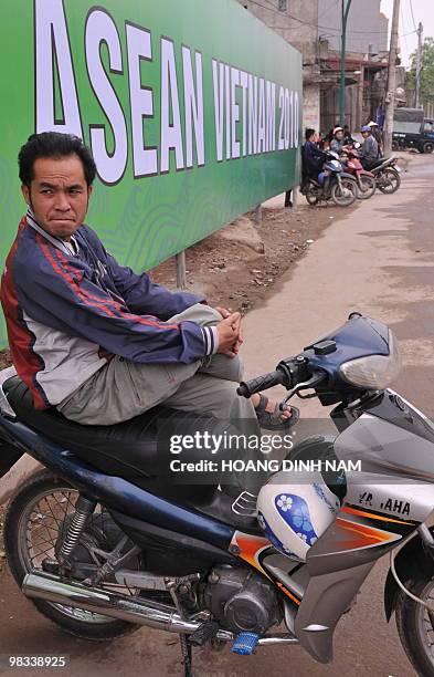 Motorcycle-taxi drivers sit waiting for clients next to a poster marking the 16th summit of the Association of Southeast Asian Nations on a road in...