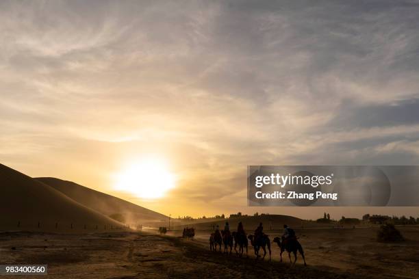 Tourists ride on camel caravans walking on Dunhuang Mingsha desert mountain. As one of famous travel destinations beside Mogao Caves in Dunhuang, not...