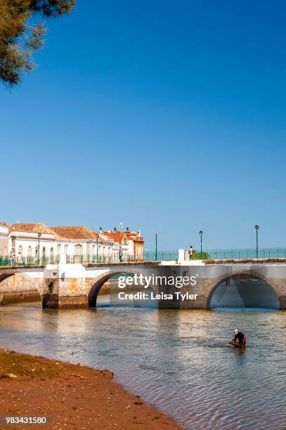 Man digging for cockles in the Gilao River next to the Roman Bridge in Tavira, a Moorish- built town on the southern coast of Portugal. The bridge is...