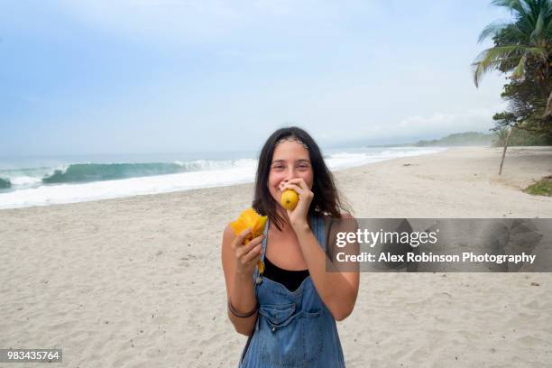 a young brunette woman traveler eating a mango on a beach - magdalena department colombia stock pictures, royalty-free photos & images