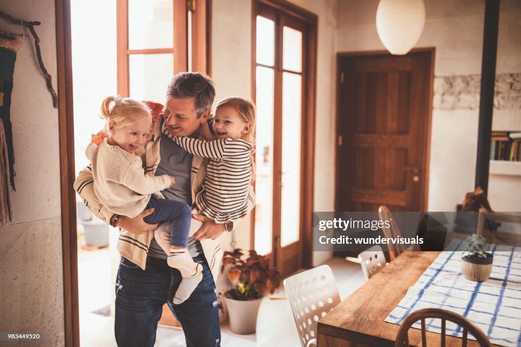 Happy father holding little daughters in his arms at home