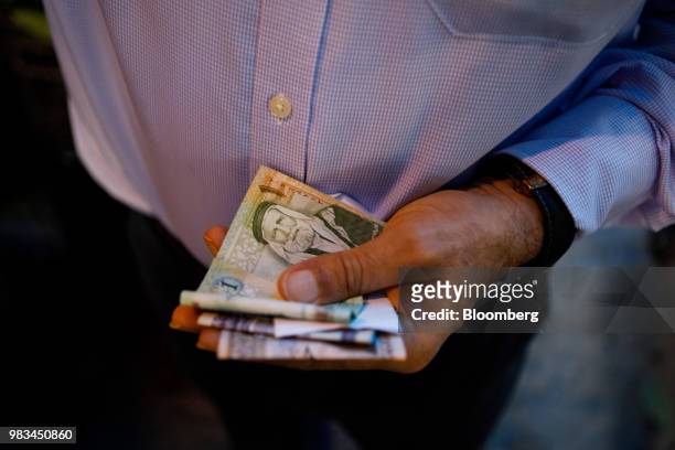 Man holds a handful of Jordanian dinar banknotes at a local fruit and vegetable market in Amman, Jordan, on Thursday, June 21, 2018. President Trump...