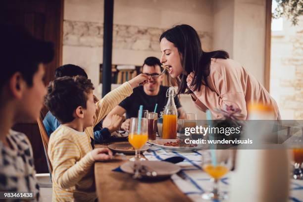 little son giving mother pancake during breakfast with family - brunch imagens e fotografias de stock
