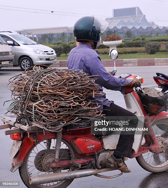 Recyclable-items trader carries used steel recovered from a construction site on her motorcyle while riding on a road near the My Dinh National...