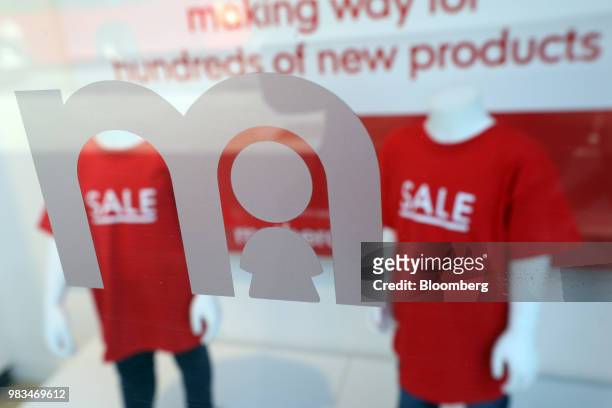 Company logo sits displayed on a Mothercare Plc store widow in front of mannequins wearing 'sale' t-shirts inside a Mothercare baby and children's...