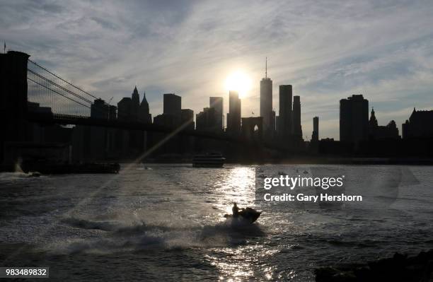 Man rides a jet ski in the East River as the sun sets behind the skyline of lower Manhttan on the summer solstice on June 21, 2018 in New York City.