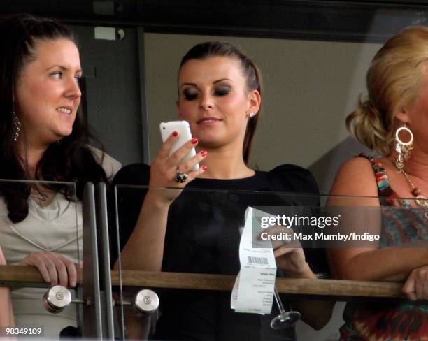 Coleen Rooney uses her iPhone as she watches the racing on 'Ladies Day' of the John Smith's Grand National horse racing meet at Aintree Racecourse on...