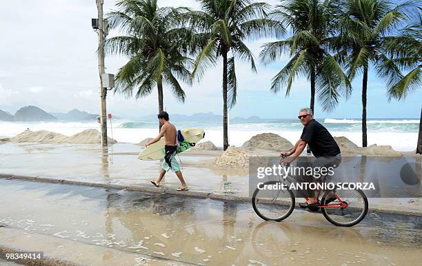 Surfer and a man in a bike circulate along the flooded sidewalk of Rio de Janeiro's Copacabana beach on April 9, 2010. The unusual roughness seen...