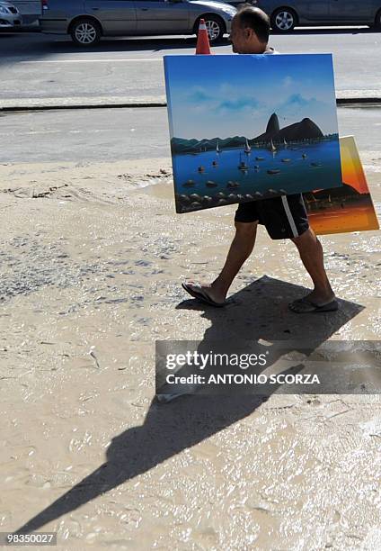 Vendor carries his picture of the Guanabara Bay, as he walks along the sidewalk of Rio de Janeiro's Copacabana beach, flooded by the high swell, on...