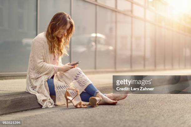 attractive woman sitting on the kerb of a street - kerb stock-fotos und bilder