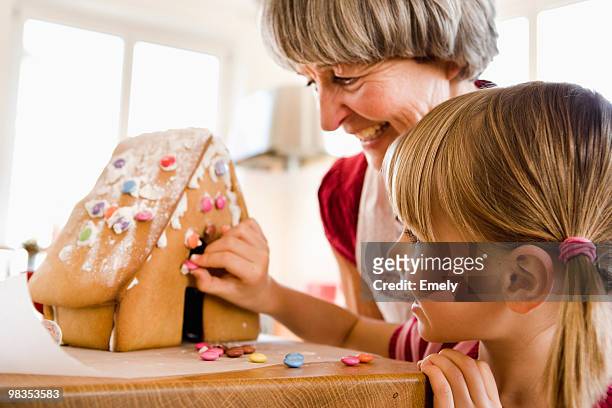 grandma and grandchild baking cake - gingerbread house stockfoto's en -beelden