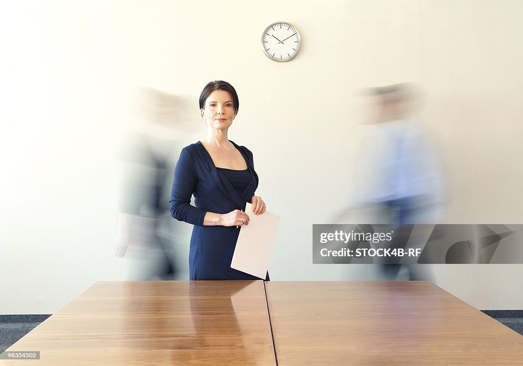 Businesswoman in conference room with people in background passing by