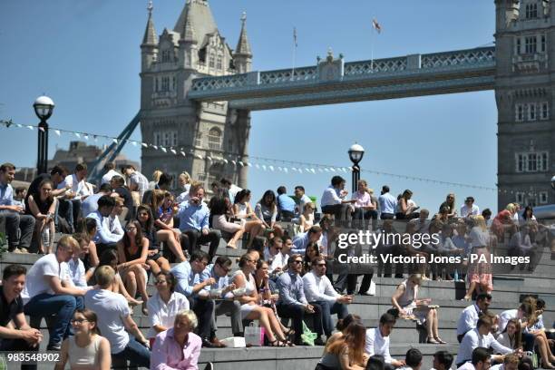 People enjoy their lunch break in the sunshine near Tower Bridge in London.