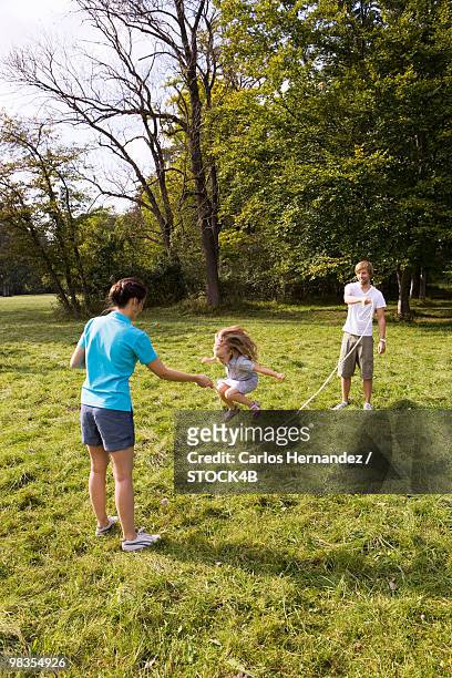 parents and daughter skipping rope in meadow, munich, bavaria, germany - skip stockfoto's en -beelden