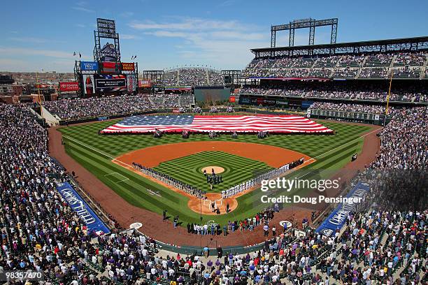 Players and fans observe the national anthem as the stars and stripes is presented by members of the US military as the Colorado Rockies host the San...