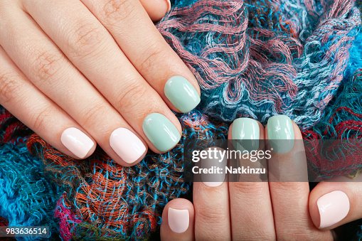 Hands with short manicured nails colored with pink and green nail polish Hands with short manicured nails colored with pink and green nail polish