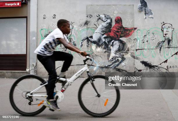 Young person goes by his bike in front of a recent artwork attributed to street artist Banksy on June 25, 2018 in Paris, France. Six frescoes,...