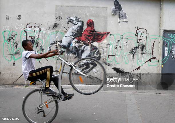 Young person goes by his bike in front of a recent artwork attributed to street artist Banksy on June 25, 2018 in Paris, France. Six frescoes,...