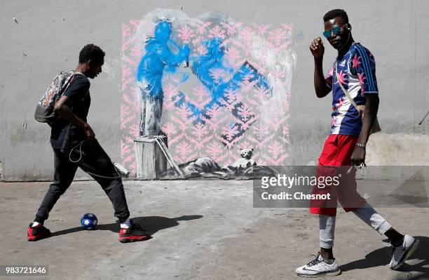 Young people play football in front of a damaged recent artwork attributed to street artist Banksy on June 25, 2018 in Paris, France. Six frescoes,...