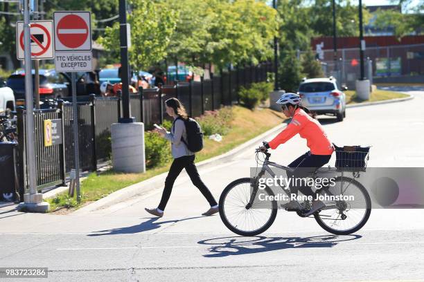 Pedestrian walks past the TTC driveway at Danforth and Woodbine in the east side of Toronto while looking at her phone as a cyclist rides by. June...