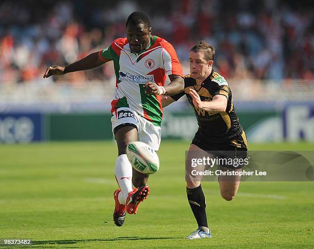 Takudzwa Ngwenya of Biarritz kicks the ball as Shane Williams of Ospreys comes in to tackle during the Heineken Cup Quarter Final match between...