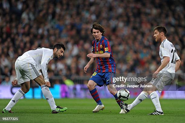 Lionel Messi of FC Barcelona passes the ball in between Raul Albiol and Xabi Alonso of Real Madrid during the La Liga match between Real Madrid and...