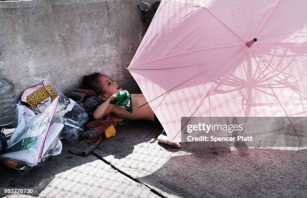 Honduran child rests under an umbrella with her mother while waiting along the border bridge after being denied entry into the Texas city of...