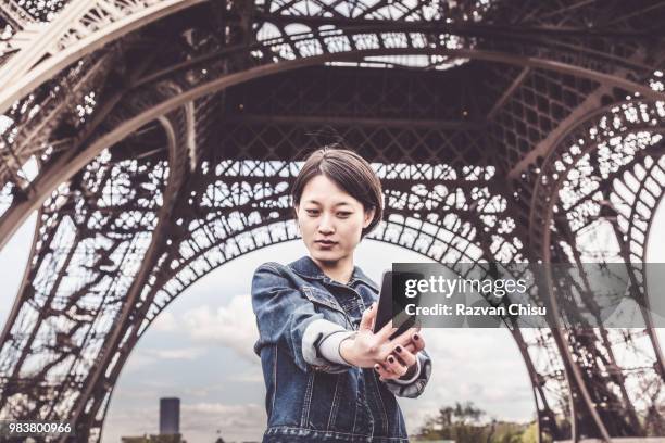 young chinese female tourist in front of the eiffel tower - chinese tower stock pictures, royalty-free photos & images