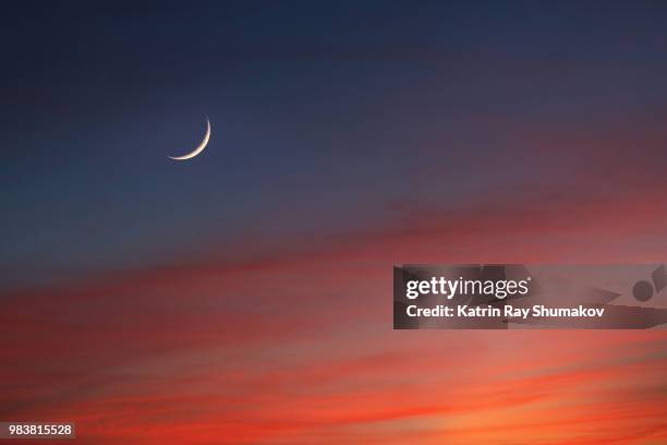 crescent moon in glowing sunset skies - red sky stock-fotos und bilder